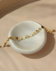 14k gold fill Starlight Bracelet laid on a white plate in the sunlight.This bracelet features a circle like chain linked together. - Token Jewelry