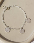 925 sterling silver Birth Flower Charm Bracelet laid on a tan plate in the sunlight. This Bracelet feature the Carter chain with as many birth flower charms as you want.