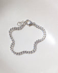 925 sterling silver cuban style chain link bracelet, laid out on a curvy ceramic dish