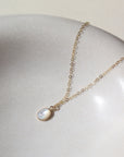 mother of pearl bezel pendant on a 14k gold fill delicate chain, photographed on a white ceramic dish