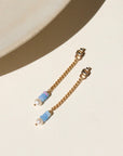 A 14k gold fill back drop with a dainty curb chain, with three opal gemstones and one mini pearl set at the bottom, the earrings are displayed on a cream backdrop in the sunlight.