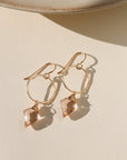 Gold earrings with rose quartz stones on a beige surface