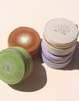 A collection of mini travel jewelry cases with embroidered sun designs, stacked together. They come in beige, green, brown, and purple colors.