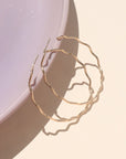14k gold fill hoop with wave-like textured wire, displayed on a cream backdrop in natural sunlight