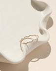 14k gold fill ring with wave-like textured wire, displayed on a cream dish in natural sunlight