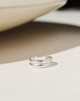 A sterling silver double layered ear cuff, displayed on a cream back drop in the sunlight