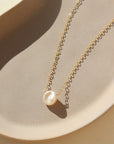 14k gold fill freshwater pearl necklace laid on a peach colored plate. This necklace features the simple chain with the freshwater pearl wired in the middle.