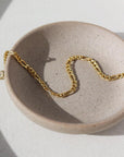 14k gold fill Gigi Bracelet laid on a gray plate set in the sunlight.