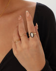 Close-up of gold-filled stacking rings and large black mother of pearl ring with a floral band on a plain background