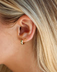 Close-up of a person wearing a gold hoop earring with blonde hair.