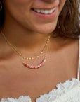 Close-up of a woman wearing a gold necklace with pink beads, smiling.