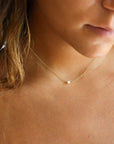 Brunette model wearing a dainty 14k gold gold fill chain featuring a mini pearl anchored in the center.