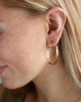 Model wearing the large pair of mirage hoops, featuring a thick hammered wire.