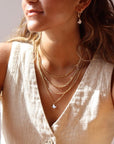 Model layering multiple chains with each other including the Delaney, Gigi, sunny, and the flutter necklace