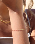 Model wearing 14k gold fill dot + dash bracelet. This is a gold bar link chain. Model is wearing a light purple tank top.