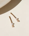 A 14k gold fill drop down post with a pearl on each ear jacket, the earrings are displayed on a cream back drop in the sunlight.