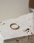 14k gold fill Spiral Ear Cuff laid on a stone plate in the sunlight. This ear cuff features the spiral allusion of a twist of two metals. This ear cuff is easy to wear on your ear.