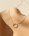 sterling silver spiral circle pendant on a a dainty sterling silver chain on a tan plate