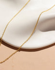 A 14k gold fill dainty chain displayed on a cream dish in the sunlight.