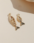 Large and small gold koi fish charms with red crystal eyes displayed on a neutral surface in warm natural light.