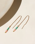 A 14k gold fill threader with two coral beads, two turquoise tubes, and one serpentine bead jumped to the bottom of each threaders, earrings are displayed on a cream backdrop in the sunlight