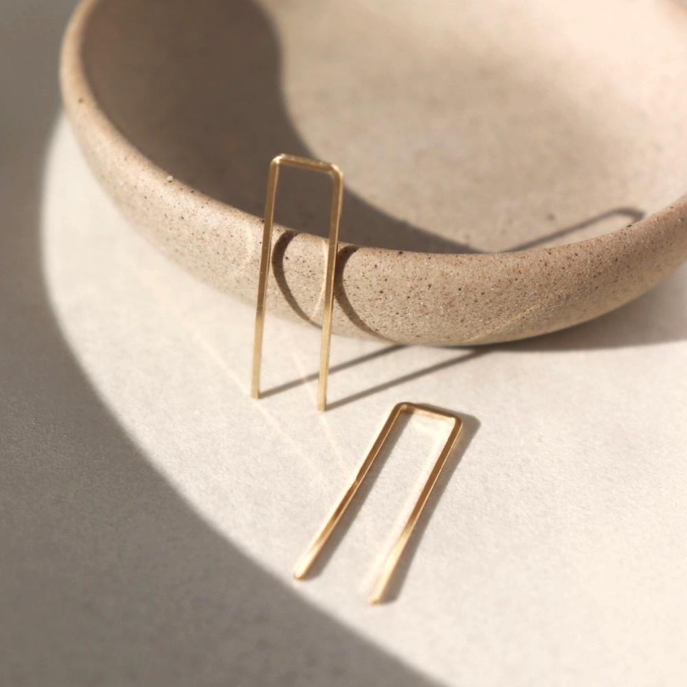 14k gold fill Staple earrings placed in the sunlight on a gray plate. A minimal earring that's perfect for everyday