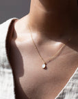 mother of pearl bezel pendant on a 14k gold fill delicate chain, photographed on a model wearing a cream linen vest