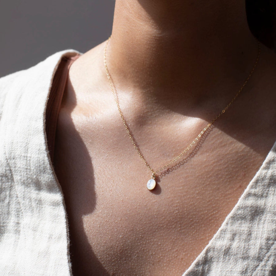 mother of pearl bezel pendant on a 14k gold fill delicate chain, photographed on a model wearing a cream linen vest