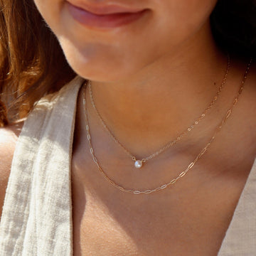 14k solid gold delicate link chain, photographed on a model layered with a pretty  round freshwater pearl hanging from a delicate cable chain.