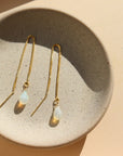 Handmade teardrop shaped faceted opals connected to a delicate box chain threader earring chain and draped over a jewelry tray in the sunlight