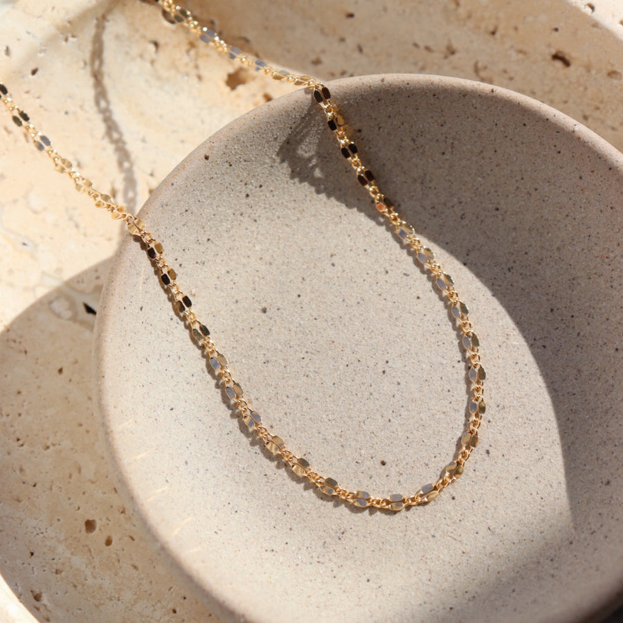 14k gold fill Scarlett chain set on a gray plate in the sunlight. This ring features delicate and feminine gold filled chain is perfect for layering or wearing solo, and its sparkly beauty is sure to make you shine!