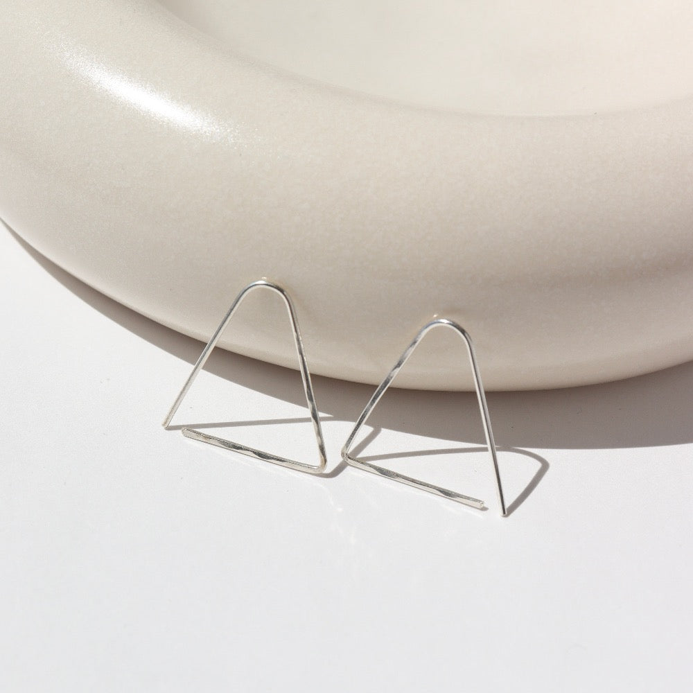 sterling silver Sunday Earrings laid on a gray plate in the sunlight. These earrings feature a triangle look easy to thread in your ear.
