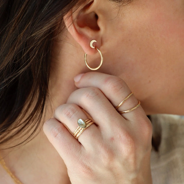 model wearing 14k gold fill rings with one 14k gold fill ring with an oval abalone stone and 14k gold fill hoops & stud earrings