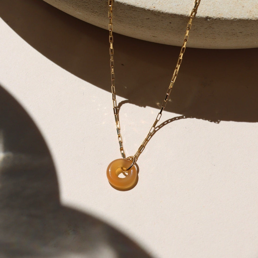 Agate donut shaped gemstone pendant attached to a 14k gold Fill chain in the sunlight