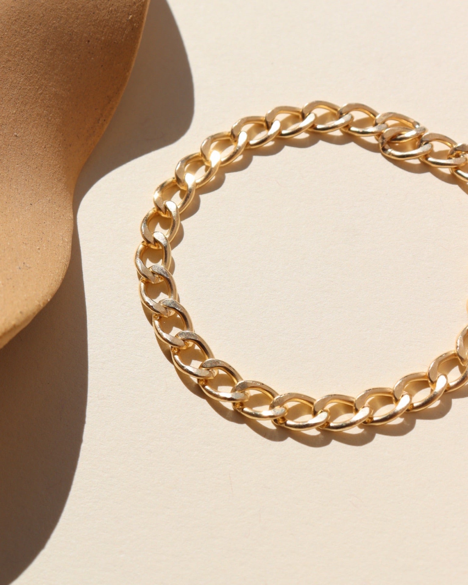 A bold curb style GF linked bracelet laid on a tan background in the sunlight
