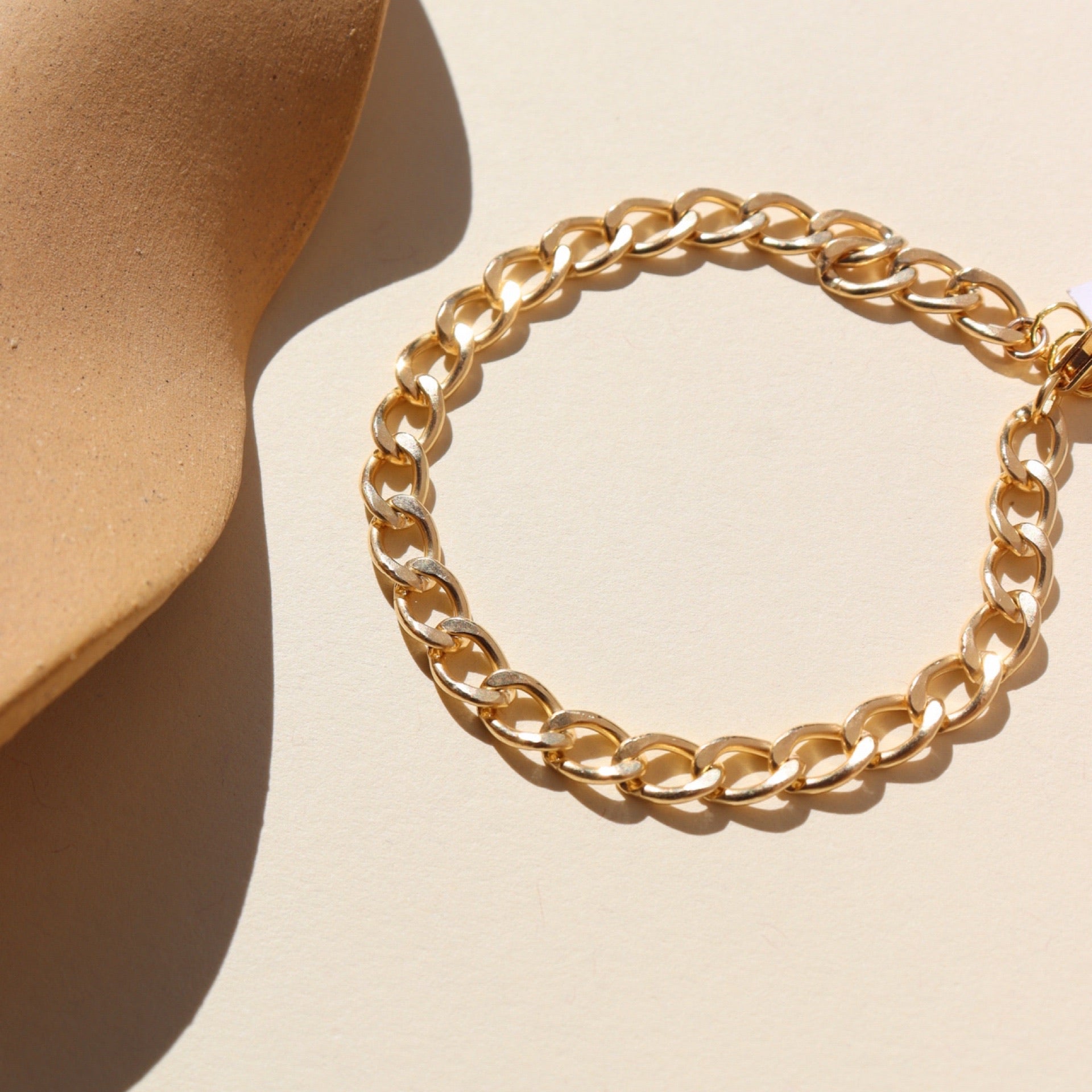 A bold curb style GF linked bracelet laid on a tan background in the sunlight