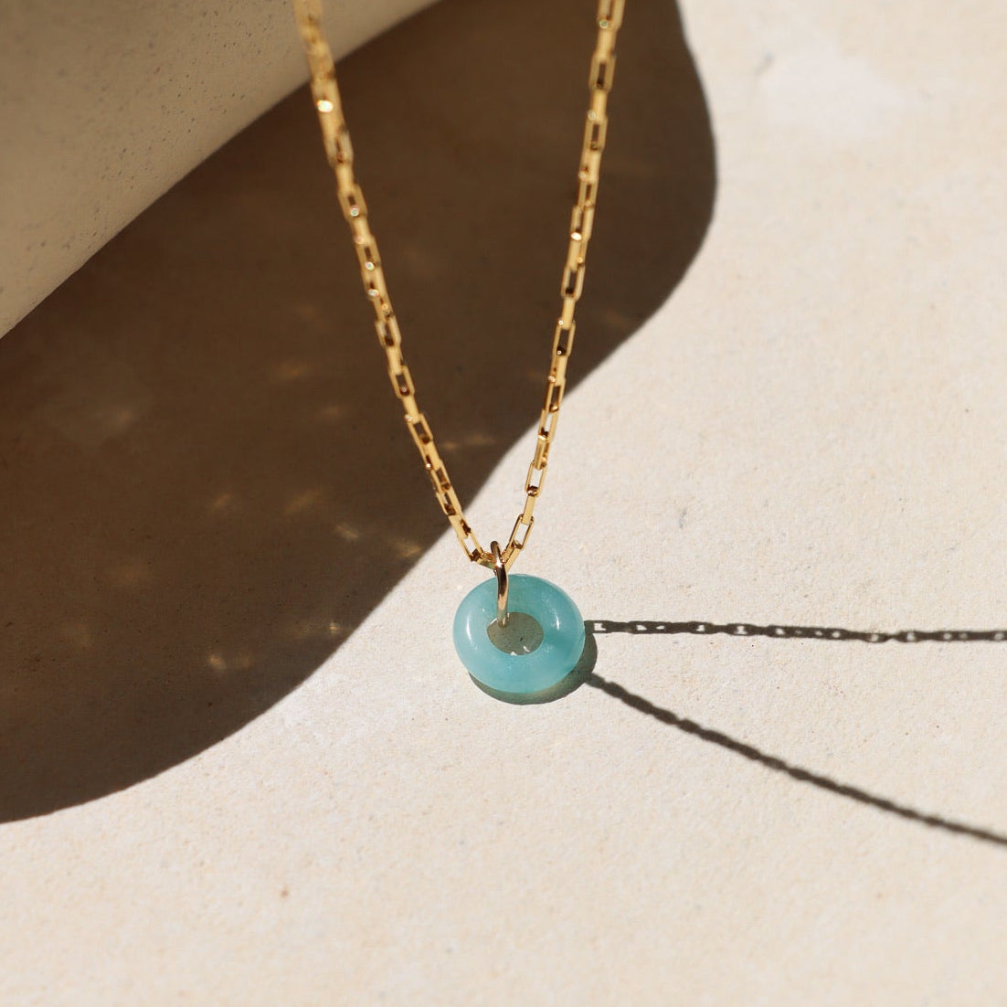 Amazonite donut shaped gemstone pendant attached to a 14k gold Fill chain in the sunlight