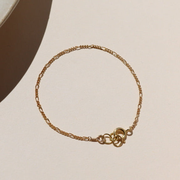14k gold fill delicate figaro chain bracelet on a light surface