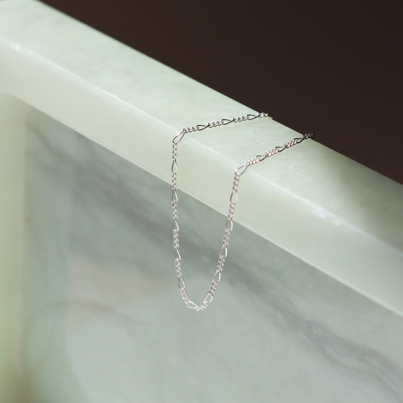 sterling silver delicate figaro chain bracelet on a light dish