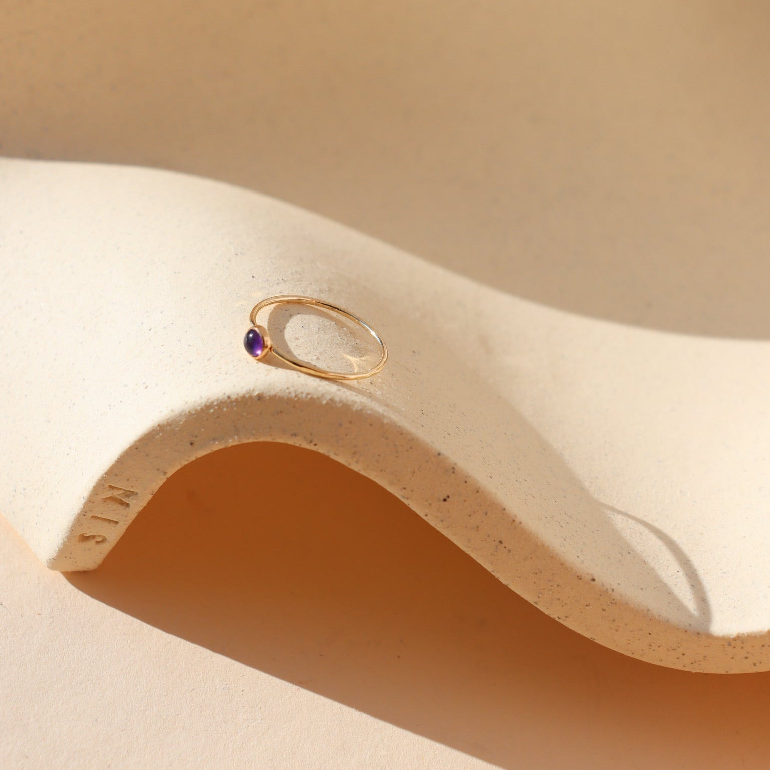 vibrant purple amethyst stone in a 14k gold fill bezel set ring on a wavy plate