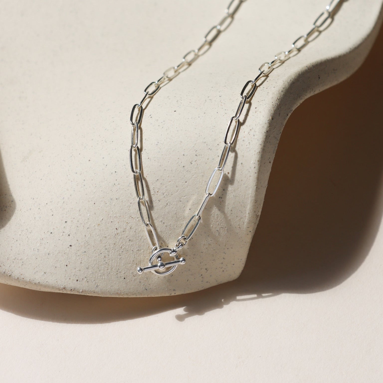 sterling silver paperclip chain necklace with toggle clasp on a light dish