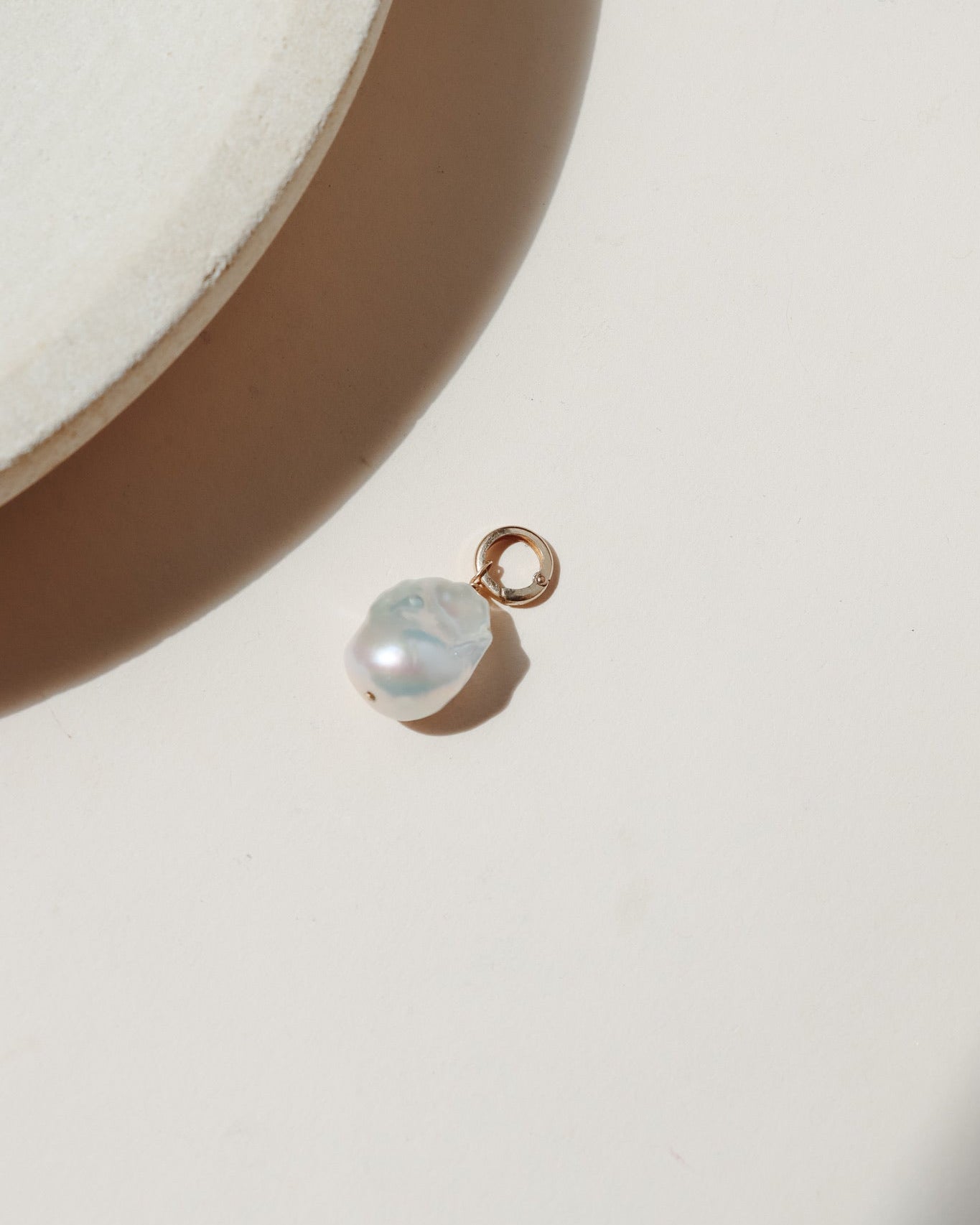 Large freshwater pearl on a round gold fill connector laid on a beige background in the sunlight