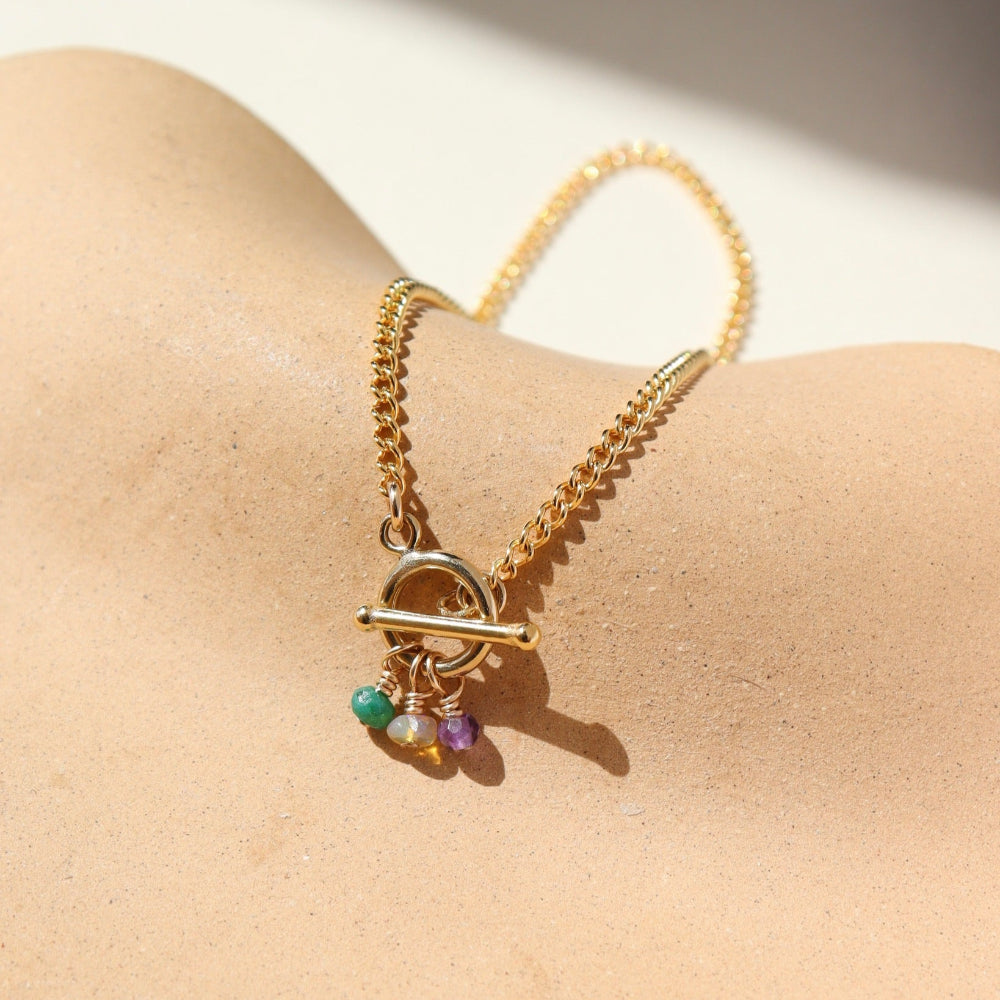 A simple 14k gold fill toggle featuring three tiny birthstone charms, dangling from a small toggle on a curb chain. The bracelet is displayed orange dish. 