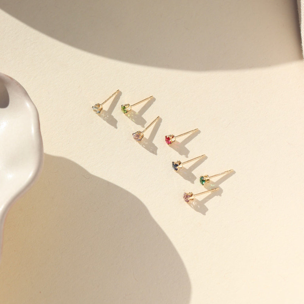 Set of gold filled birthstone prong set earrings on a beige surface with soft shadows