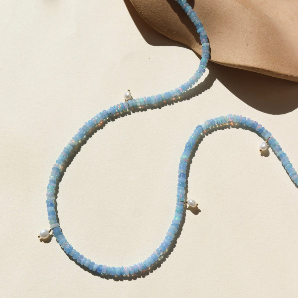 A 14k gold fill fully beaded necklace featuring blue opal gemstones and 6 freshwater pearls. The necklace is displayed on a cream back drop. 