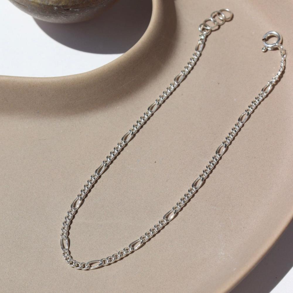 sterling silver figaro chain bracelet on a tan plate