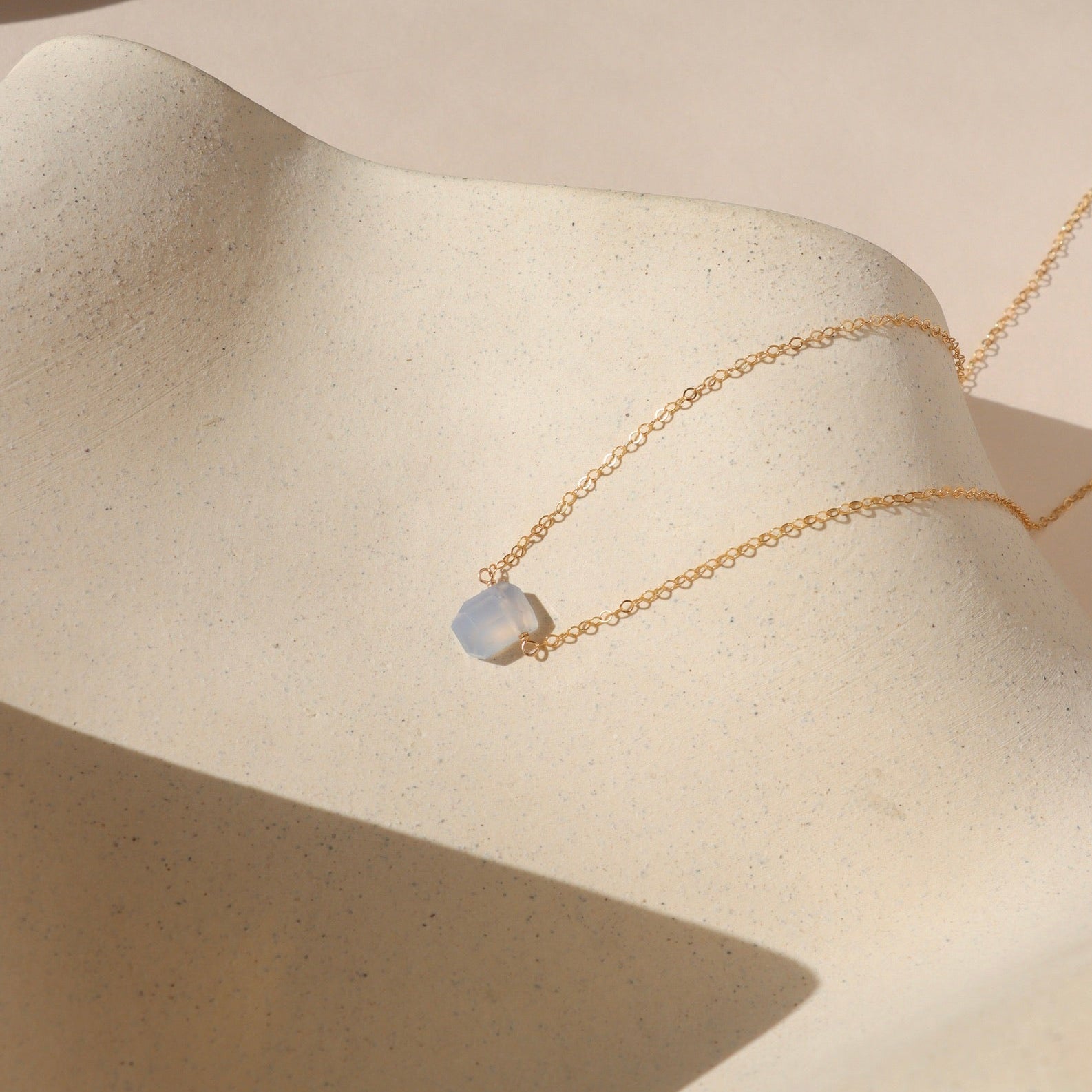 14k gold fill simple chain with chalcedony stone wrapped in the center on a light dish
