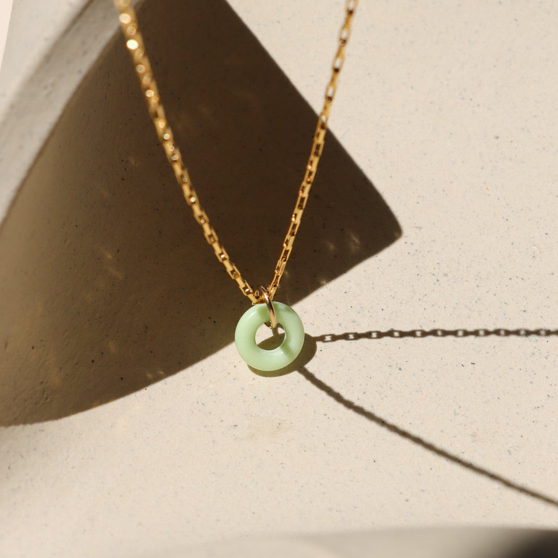 Chrysoprase donut shaped gemstone pendant attached to a 14k gold Fill chain in the sunlight