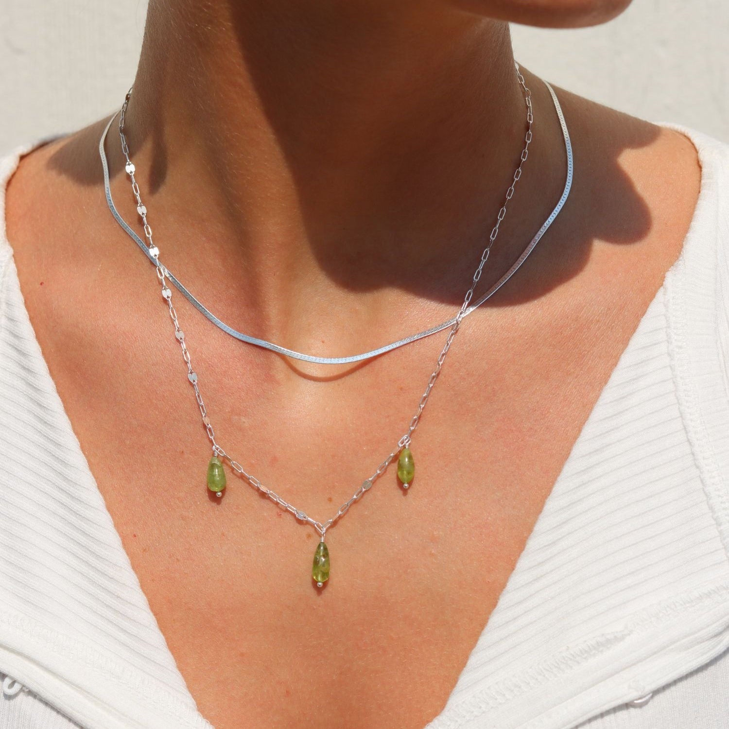 model wearing silver herringbone chain necklace with chain and pendant necklace in the sunlight