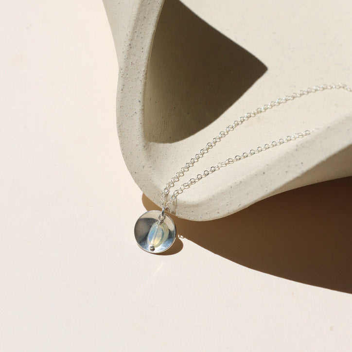 sterling silver delicate chain necklace with round charm and opal on a light dish